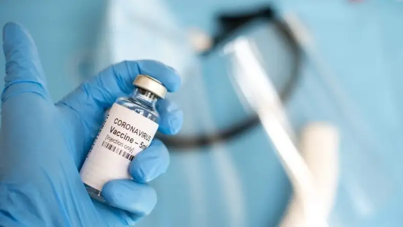 Close-up of a coronavirus vaccine vial in a blue-gloved hand