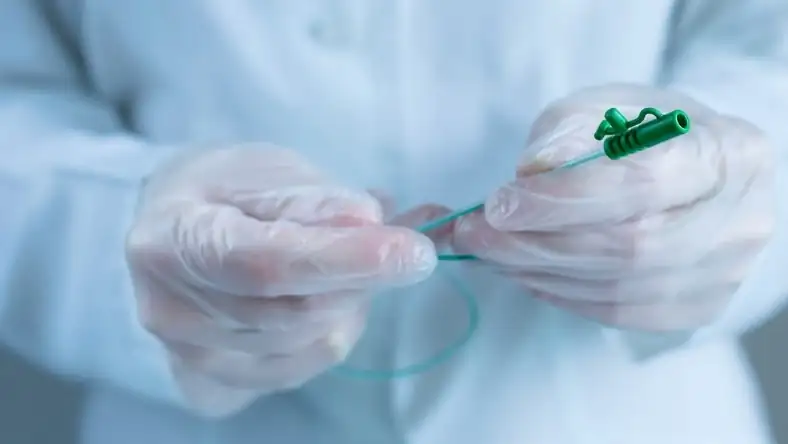 Gloved hands holding a thin medical catheter used in vascular procedures
